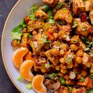 close-up of gochujang tofu and veggies in bowl over lettuce with orange pieces and sesame seeds