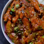 overhead close-up of crispy Indo Chinese chicken in a bowl with rice and green onions