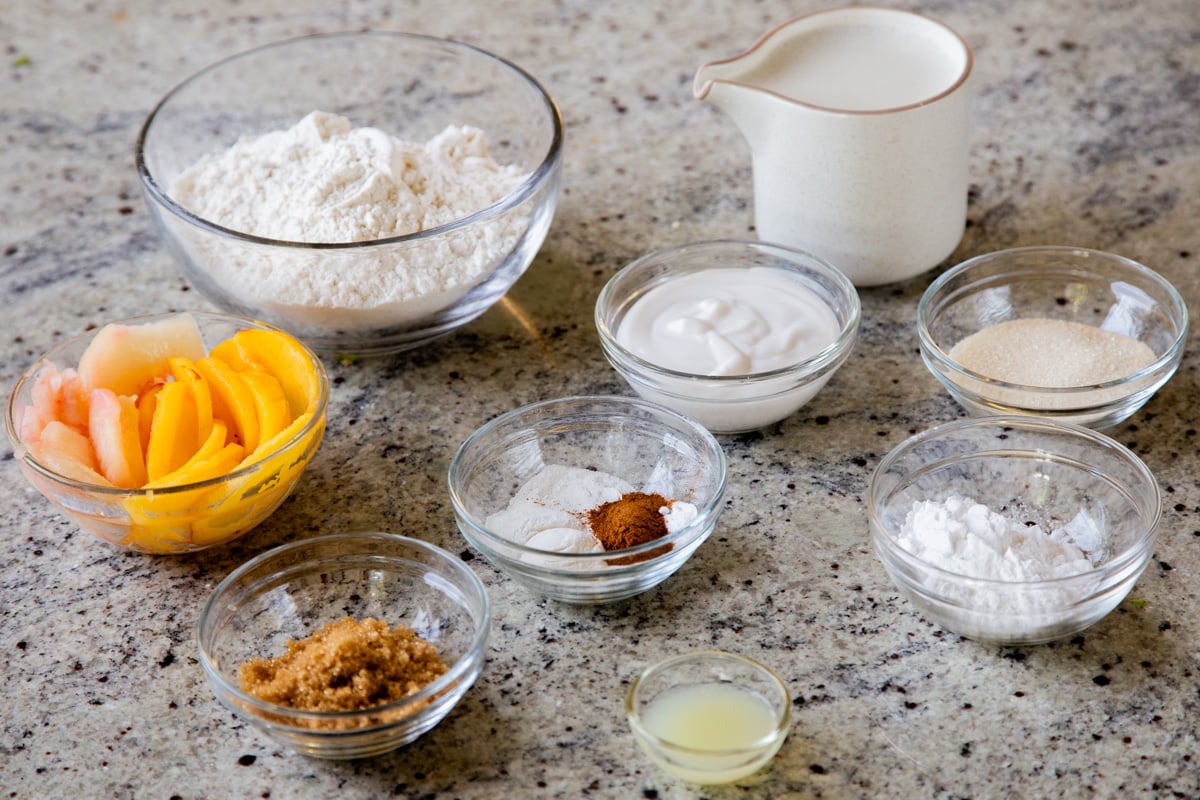 peaches, flour, and other pancake ingredients in bowls on a kitchen counter