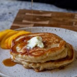 drizzling maple syrup onto a plate of peach pancakes