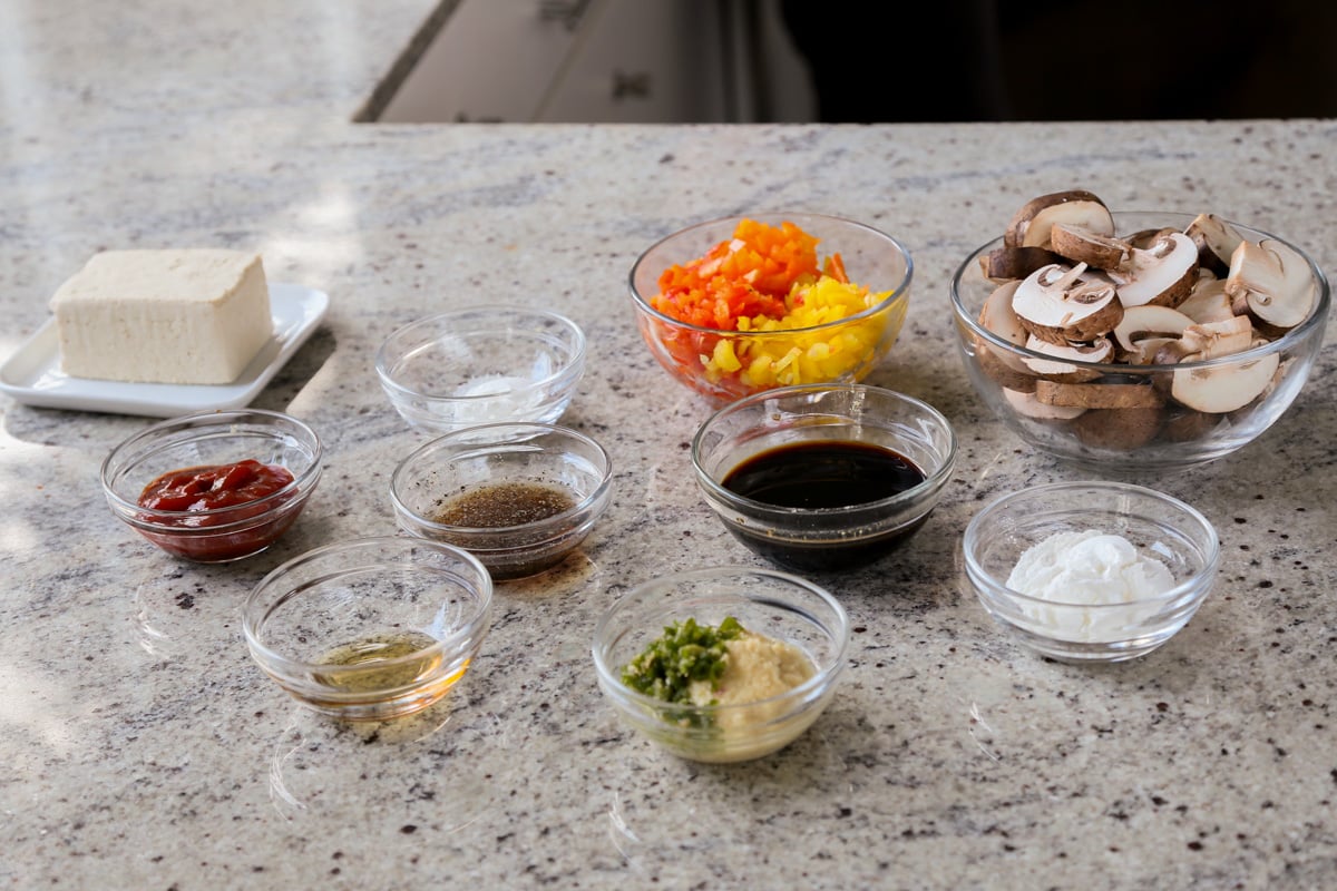 mushrooms, tofu, and other baked stir fry ingredients in bowls on a kitchen counter