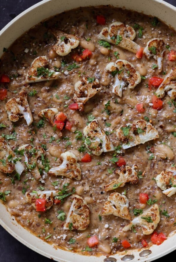 caramelized onion beans in the pan topped with charred cauliflower, tomato, and herbs