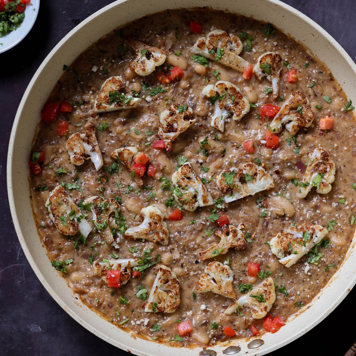 caramelized onion beans in the pan topped with charred cauliflower, tomato, and herbs