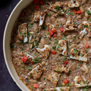 caramelized onion beans in the pan topped with charred cauliflower, tomato, and herbs