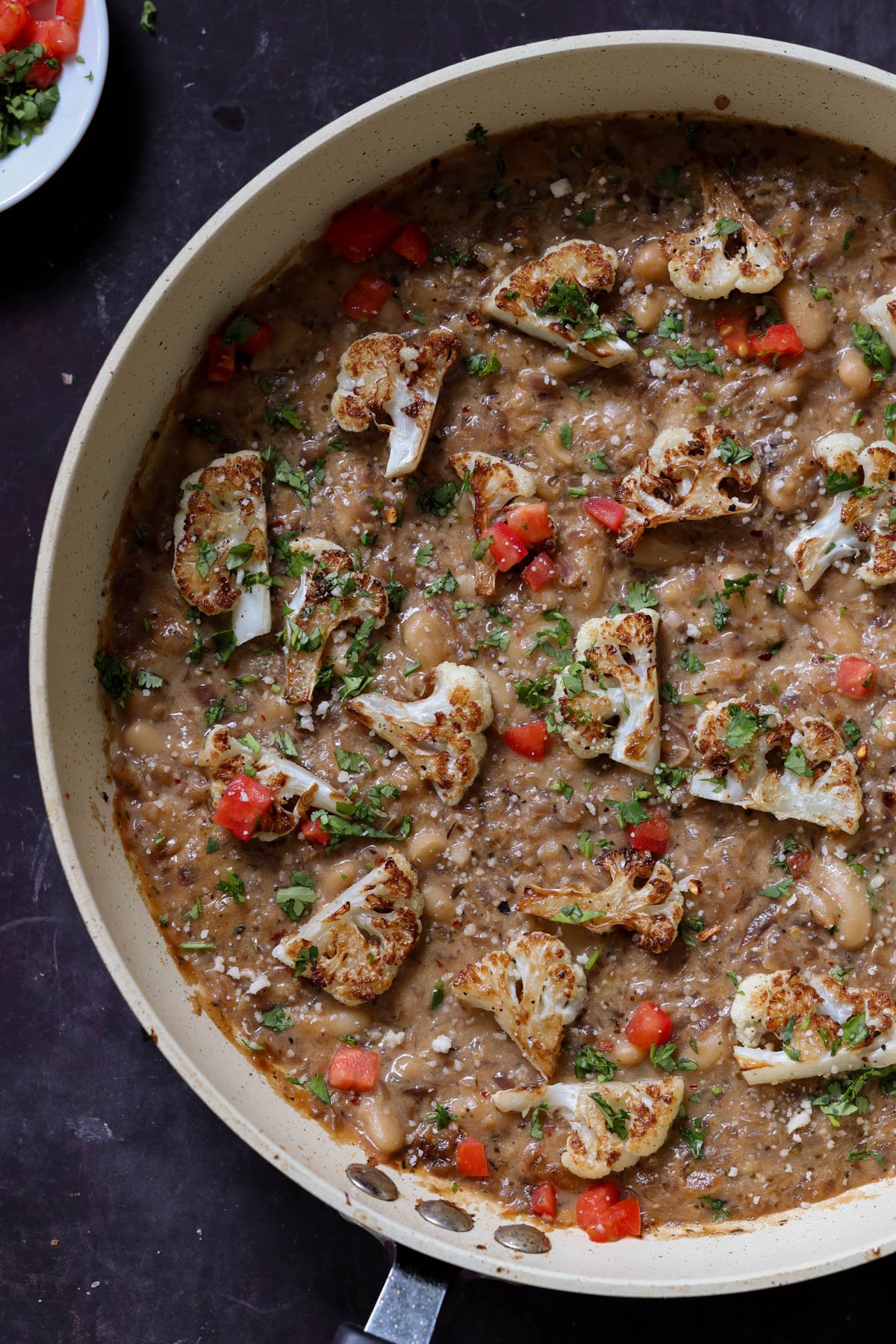 caramelized onion beans in the pan topped with charred cauliflower, tomato, and herbs