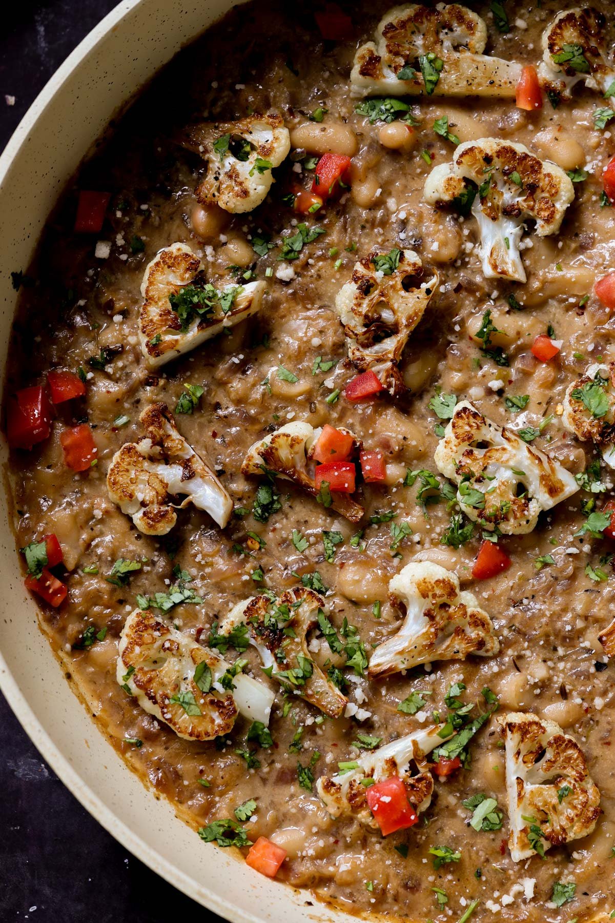 close-up of caramelized onion beans in the pan topped with charred cauliflower, tomato, and herbs