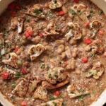 caramelized onion beans in the pan topped with charred cauliflower, tomato, and herbs