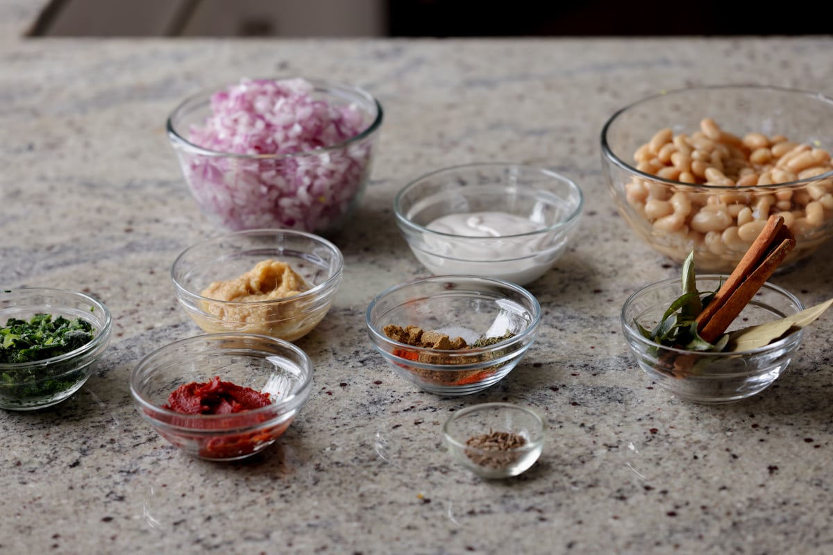 spices, tomato paste, and other Dhaba chicken white beans ingredients in bowls on a kitchen counter