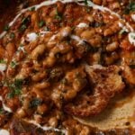 close-up of dipping sourdough into Dhaba chicken white beans