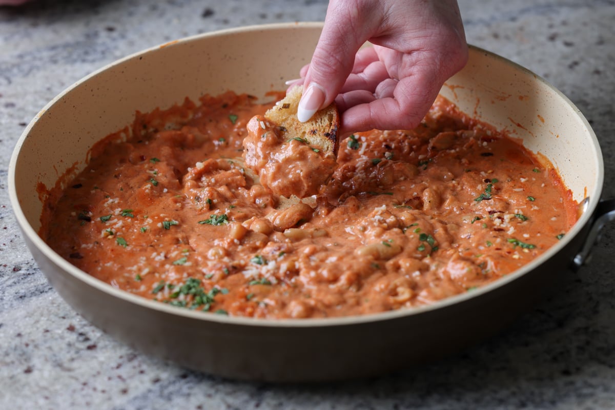dipping sourdough into rosé sauce beans in the pan