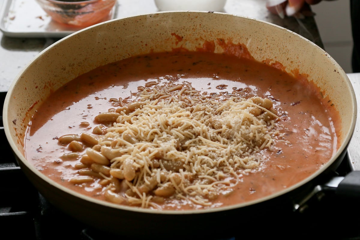 adding vegan Parmesan to rosé sauce beans in the pan