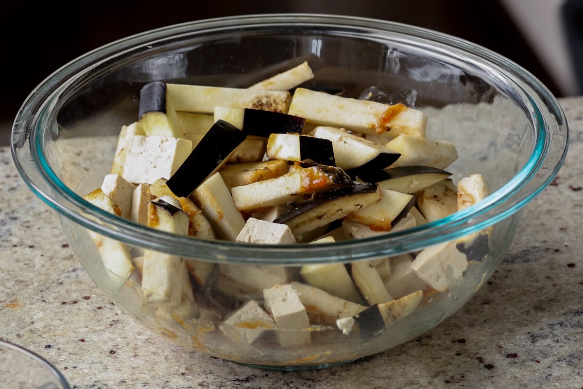adding eggplant and tofu to the bowl of sauce