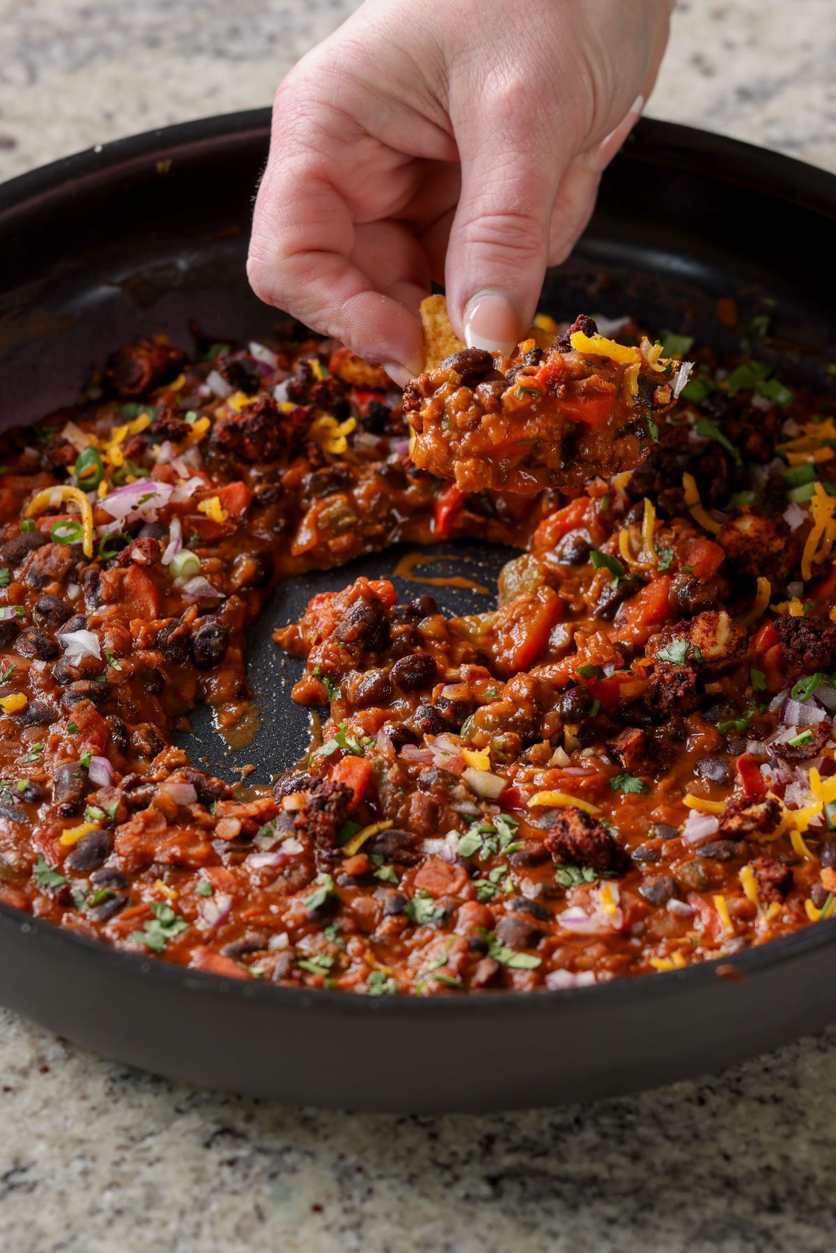 dipping a tortilla chip into the pan of black beans and lentils