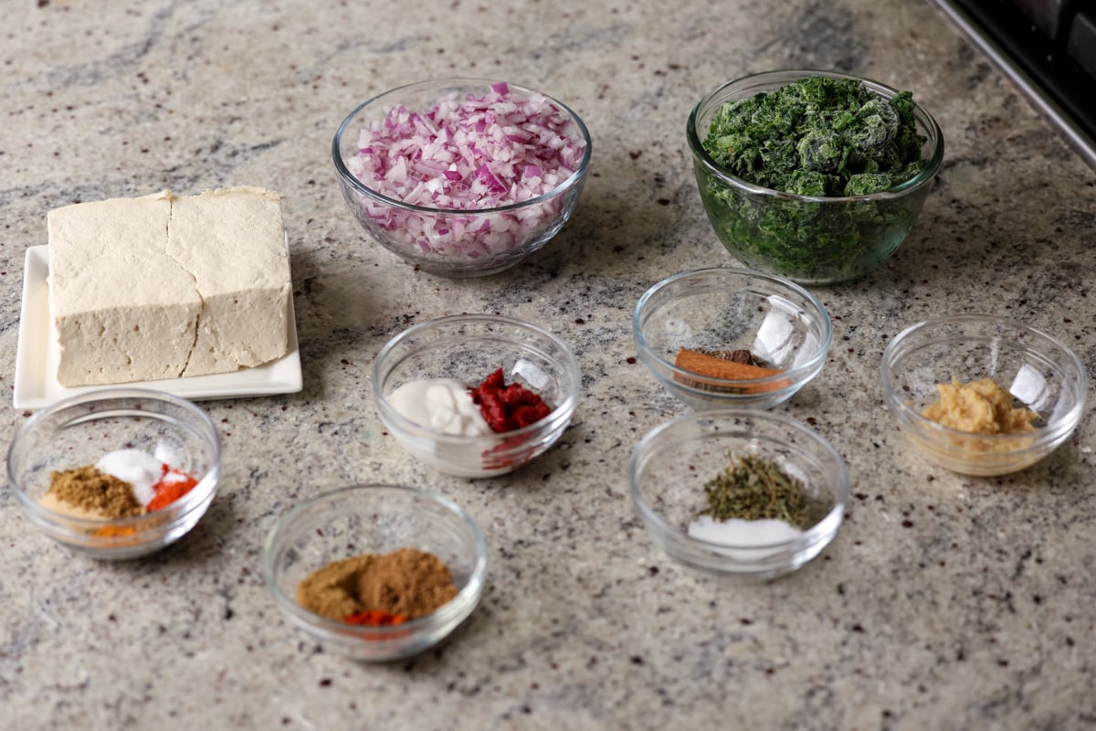 spinach, onions, spices, and other vegan chicken saagwala ingredients in bowls on the kitchen counter