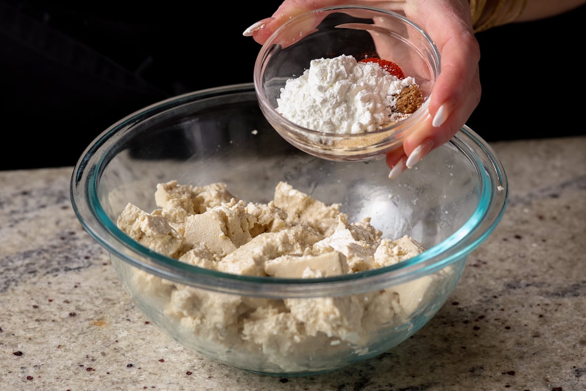 hand holding cornstarch and spices in a small bowl over the tofu