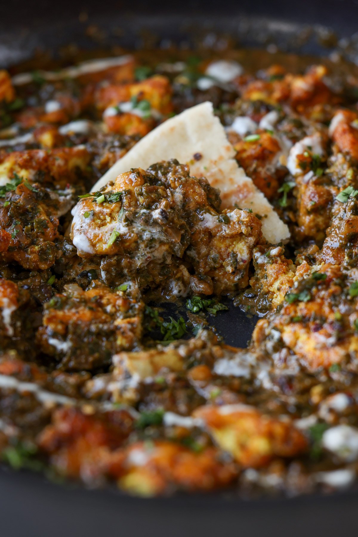 close-up of a piece of flatbread in the pan of chicken saagwala