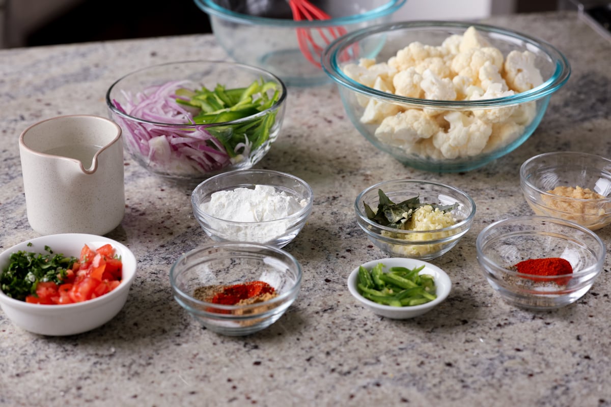 cauliflower, onions, spices, and other pepper fry ingredients in bowls on the kitchen counter