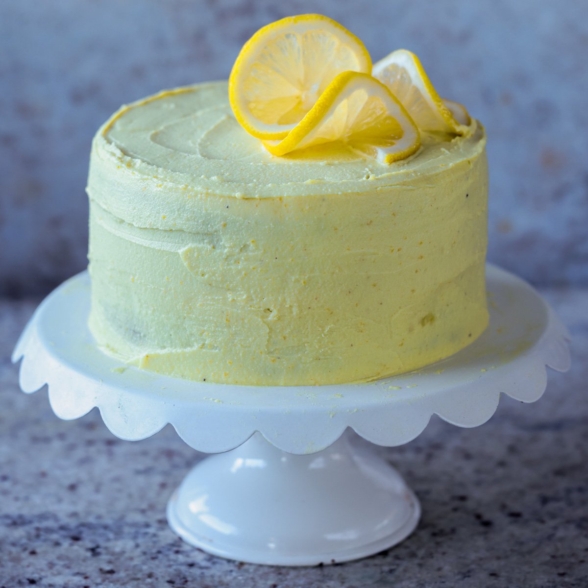 vegan lemon cake on the serving tray after frosting and topping with lemon slices