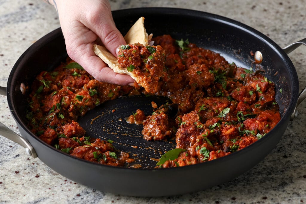 hand scooping up Madurai Chicken Curry with a piece of flatbread