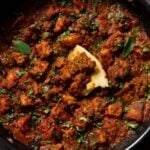 Madurai Chicken Curry in the pan with a piece of flatbread in it