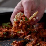 hand scooping up Madurai Chicken Curry with a piece of flatbread