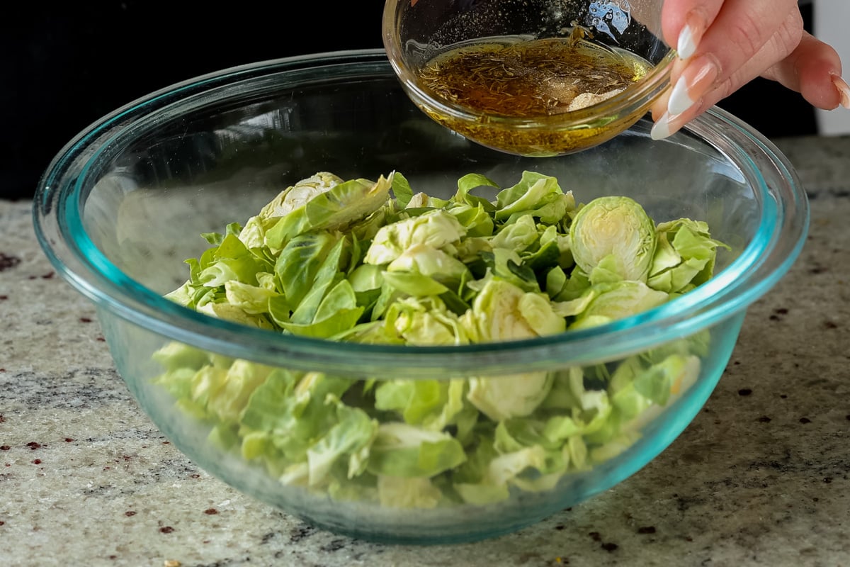mixing seasonings over the bowl of Brussels sprouts