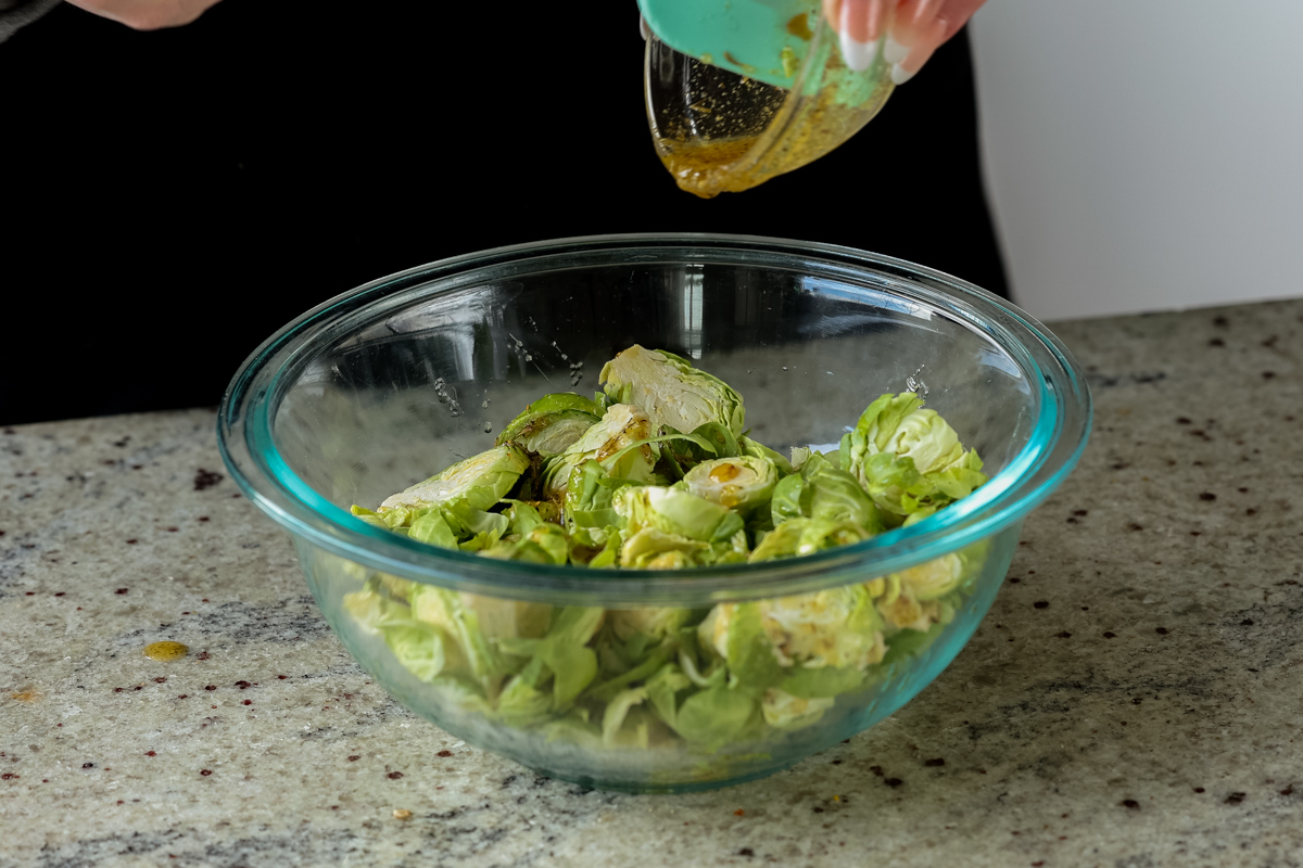 pouring seasonings onto shaved Brussels sprouts in a bowl
