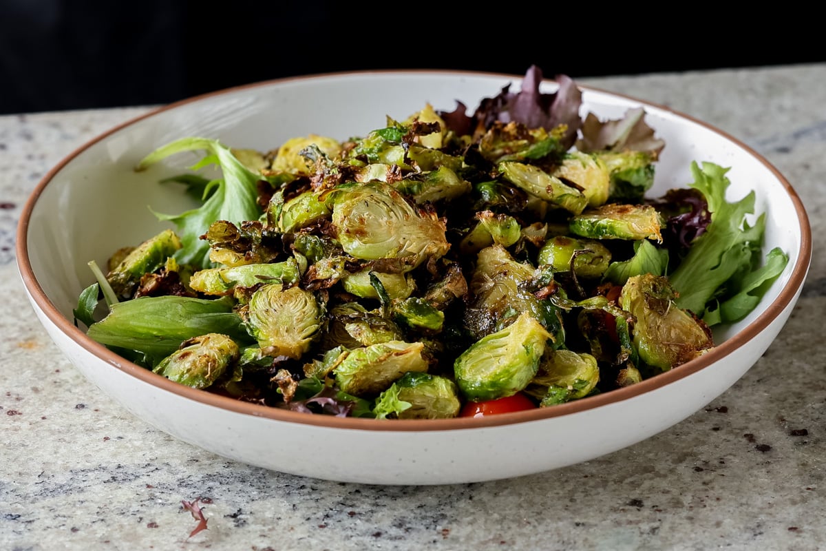 shaved Brussels sprouts salad in a bowl with tomatoes, lettuce before adding the walnut crumble