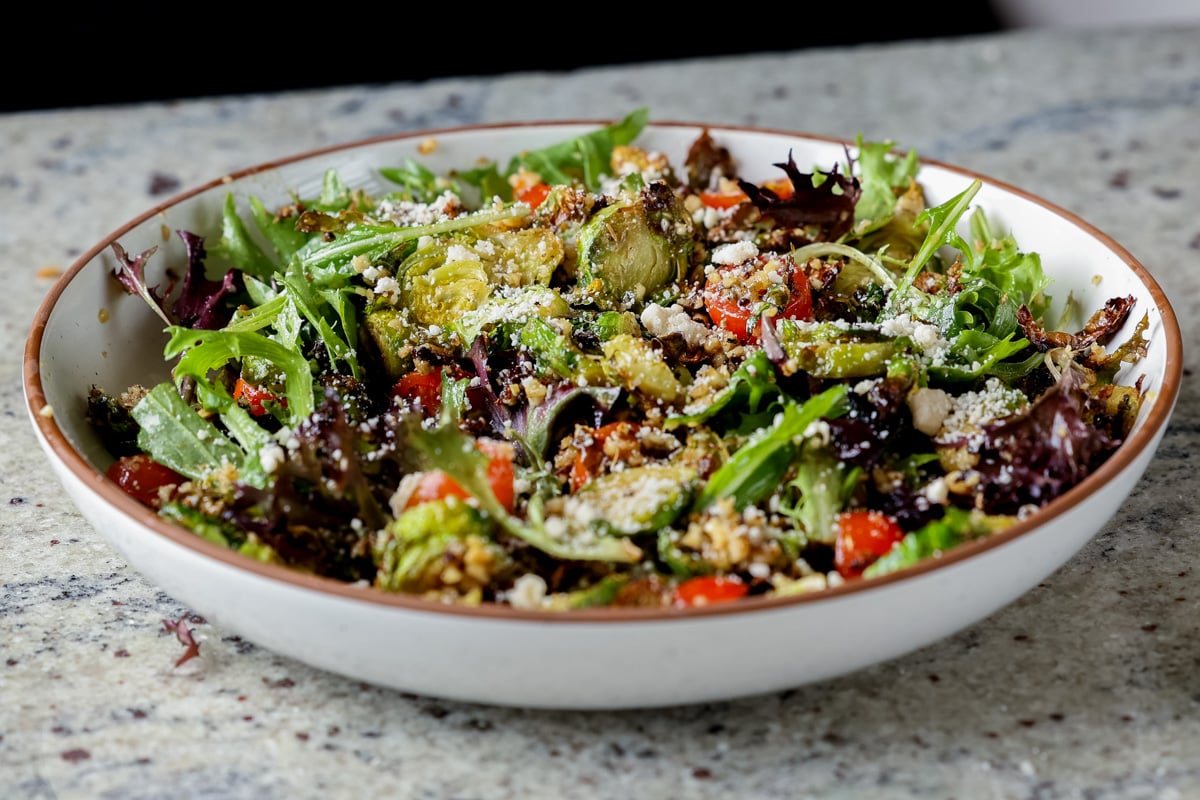 shaved Brussels sprouts salad in a bowl with tomatoes, lettuce, and walnut crumble