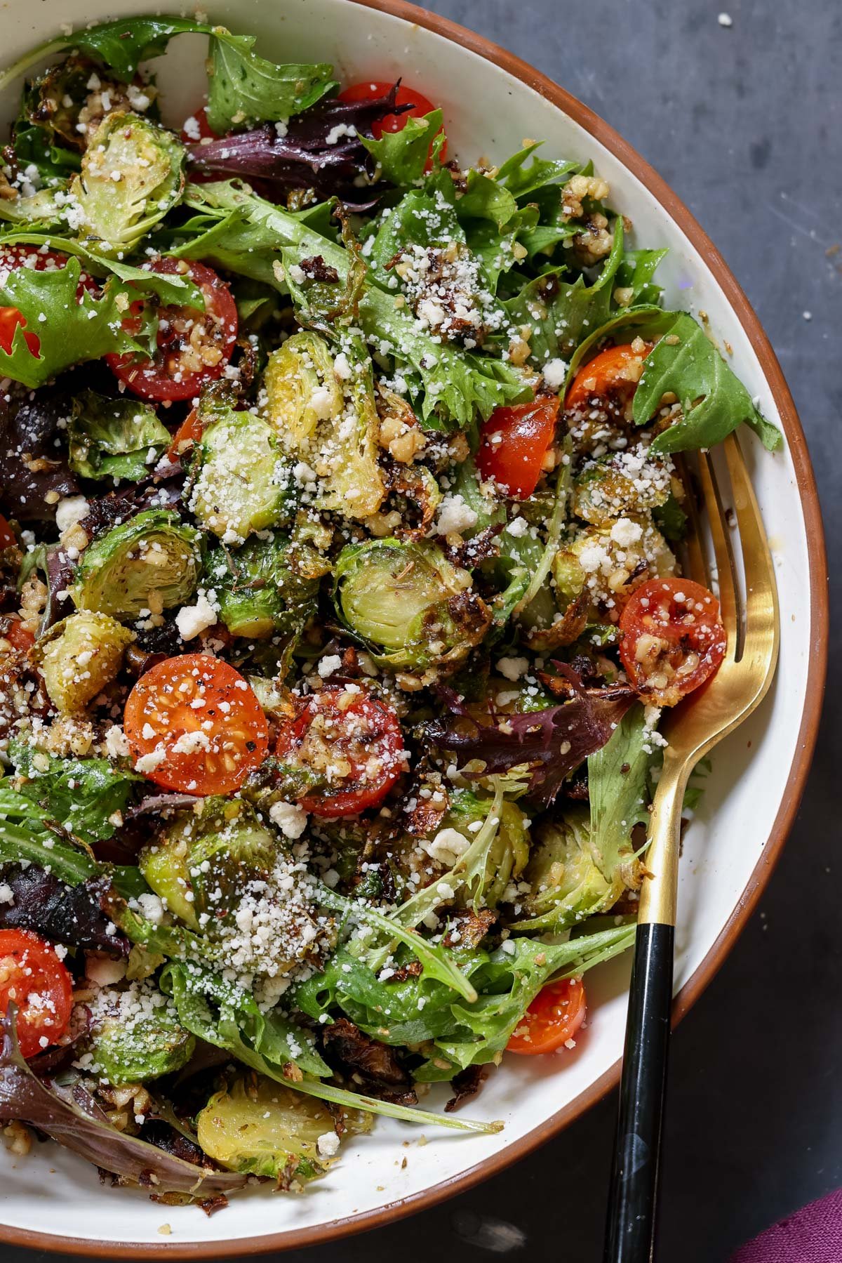 close-up of shaved Brussels sprouts salad in a bowl with tomatoes, lettuce, and walnut crumble