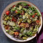 shaved Brussels sprouts salad in a bowl with tomatoes, lettuce, and walnut crumble