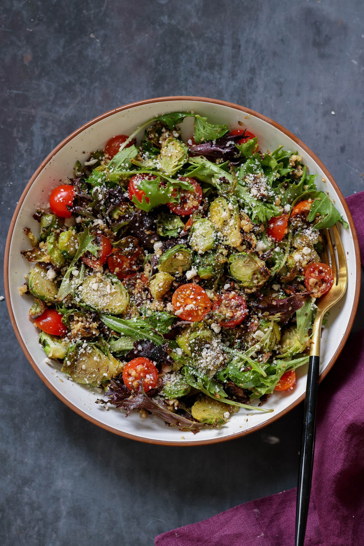 shaved Brussels sprouts salad in a bowl with tomatoes, lettuce, and walnut crumble