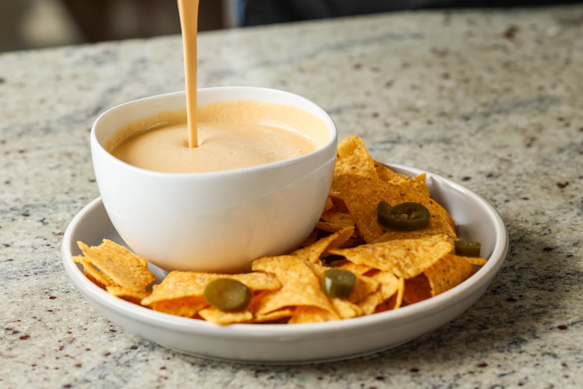 pouring cashew nacho cheese into a serving bowl