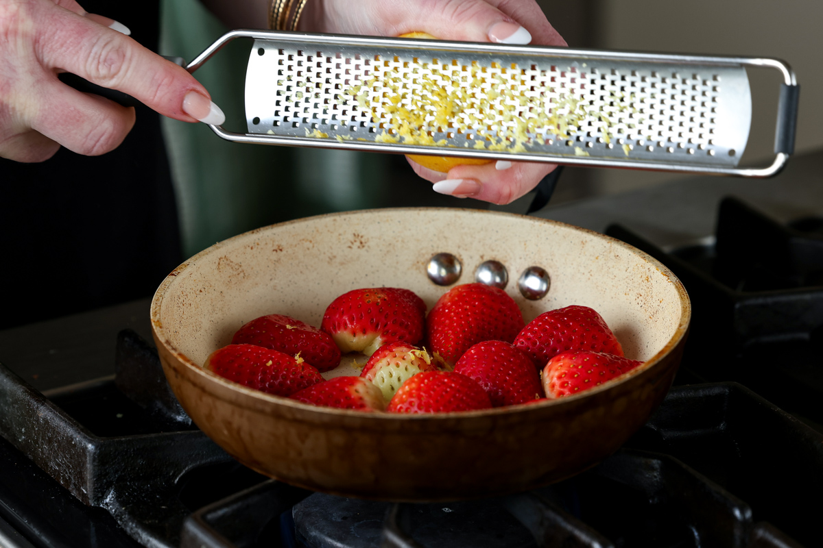 adding lemon zest to strawberries in a pan