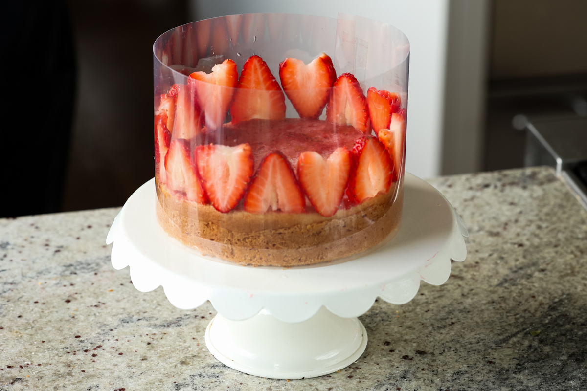arranging strawberry slices around the top of the cake inside the cake collar