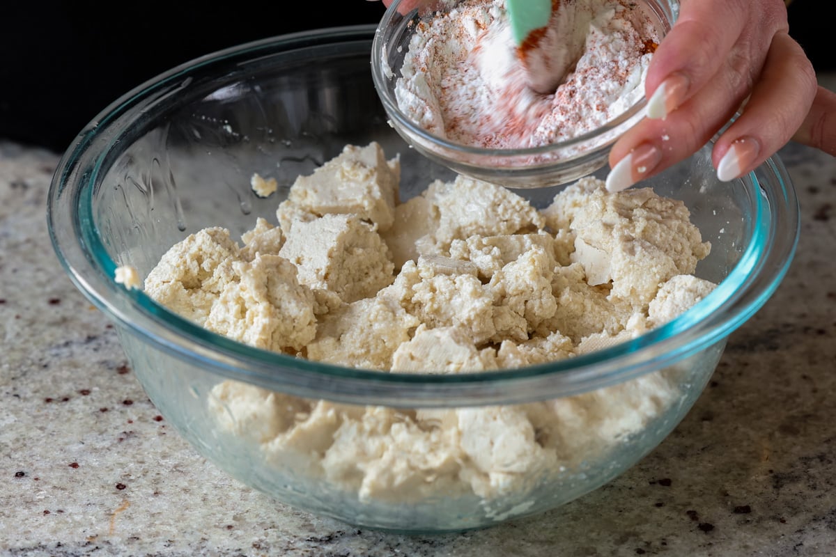mixing cornstarch and spices over the bowl of tofu