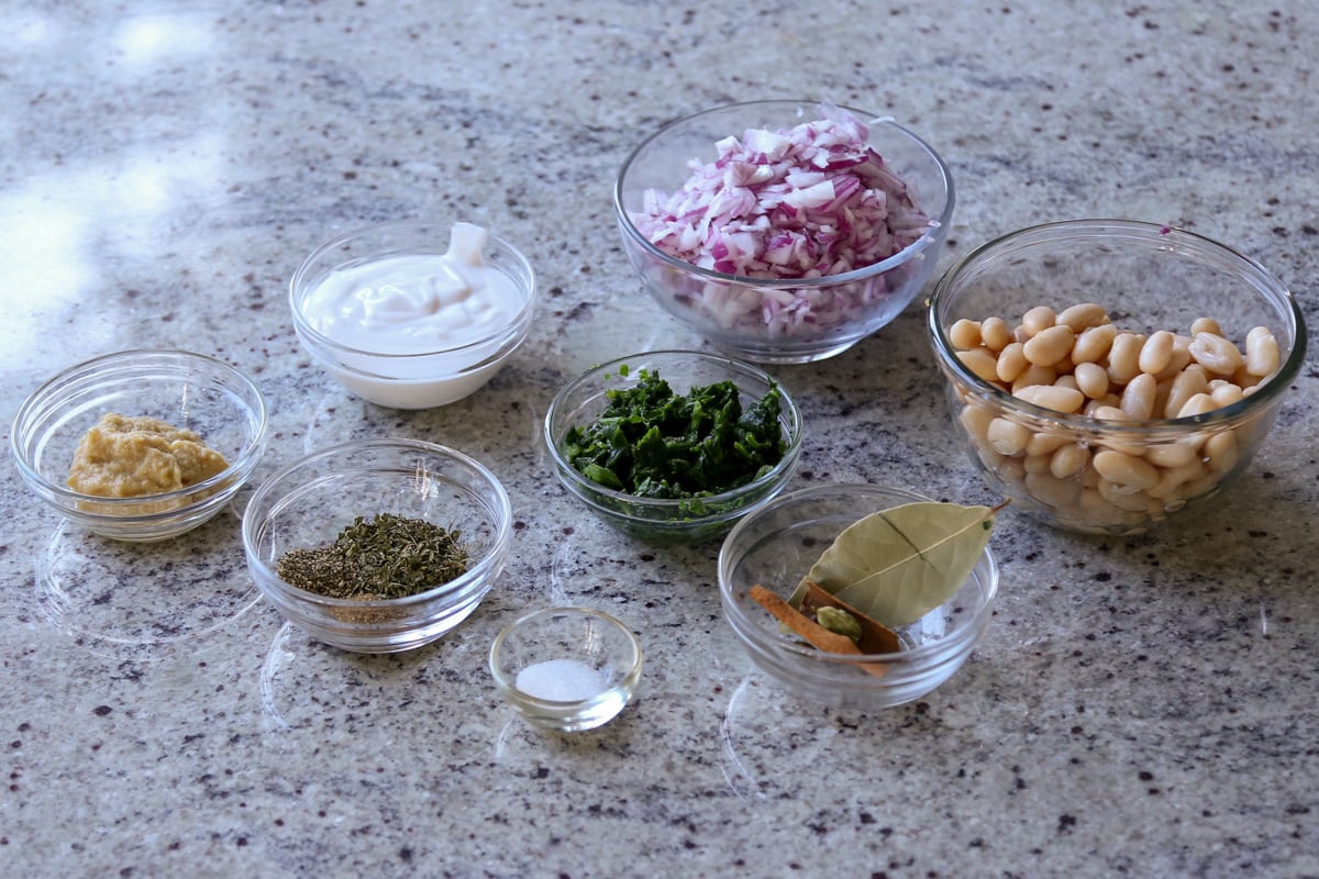 beans, spices, and other kali mirch ingredients in bowls on the kitchen counter