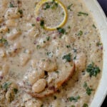 close-up of dipping bread into lemon garlic butter beans in a pan