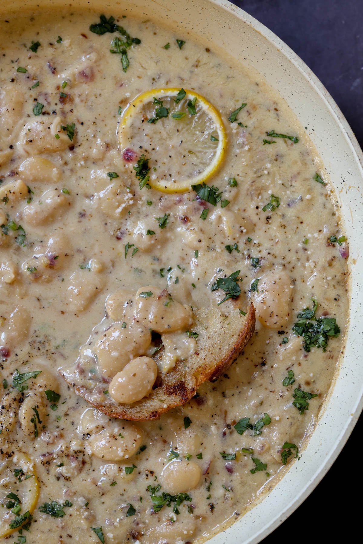 close-up of dipping bread into lemon garlic butter beans in a pan