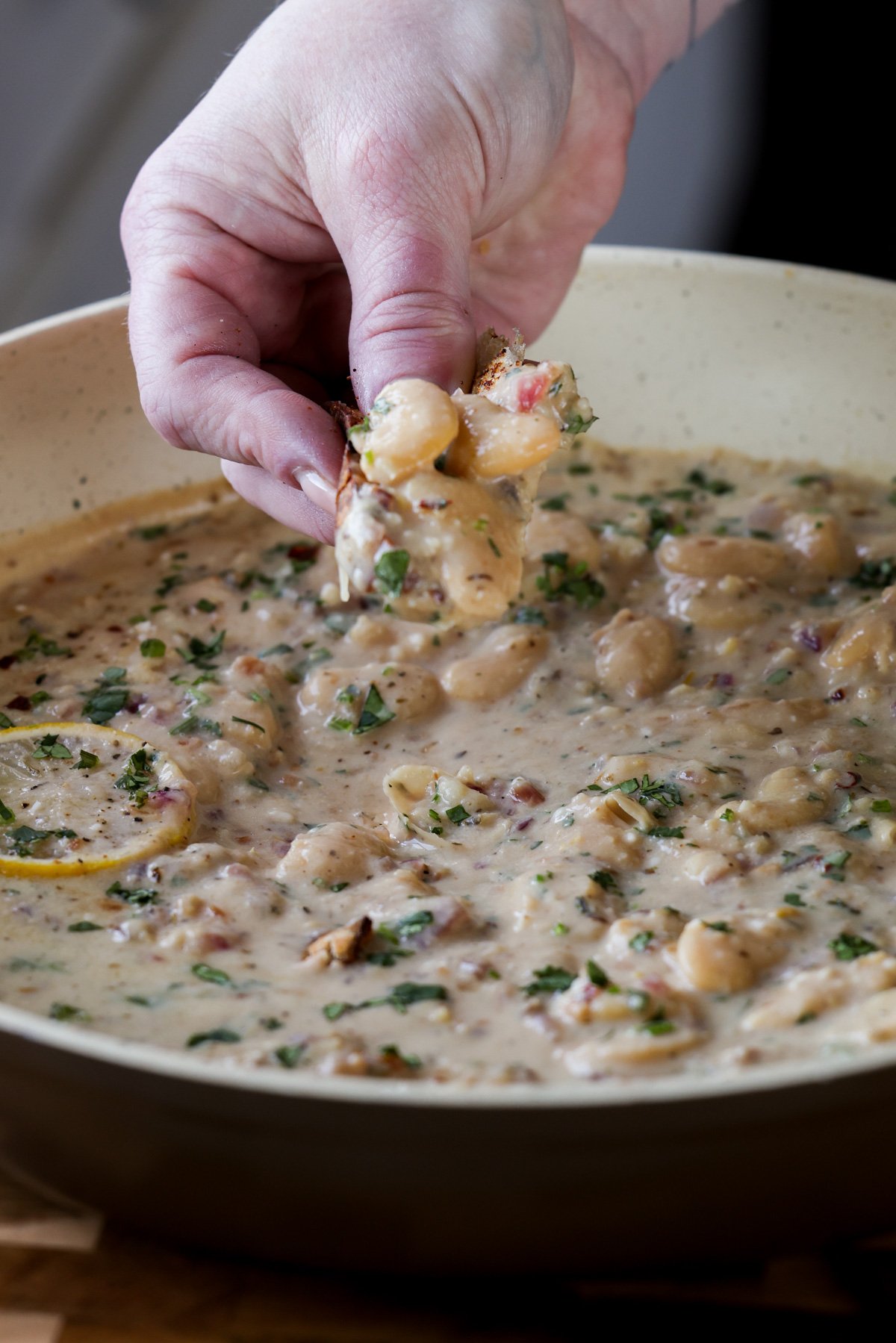 hand scooping up some lemon garlic butter beans on a piece of bread