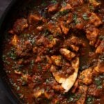 malvani chicken curry in the pan with a piece of flatbread