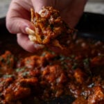 hand scooping up some malvani chicken curry using a piece of flatbread