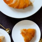 slices of peach upside-down cake on plates next to the cake on a cake stand