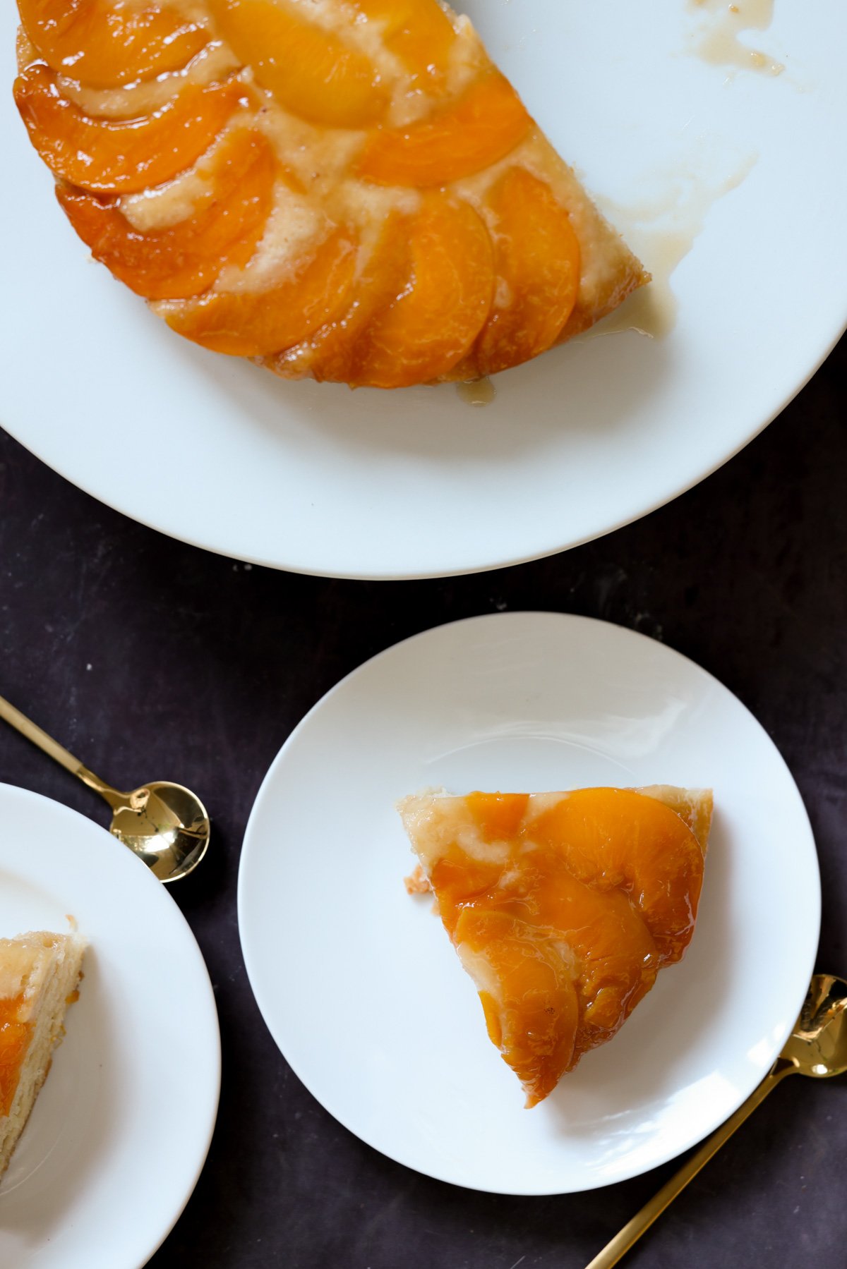 slices of peach upside-down cake on plates next to the cake on a cake stand