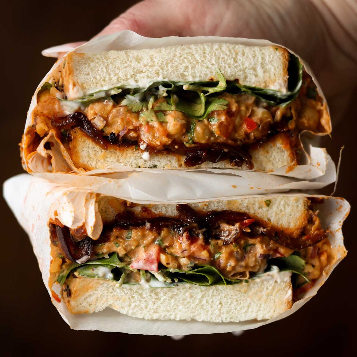 hand holding a gochujang chickpea salad sandwich