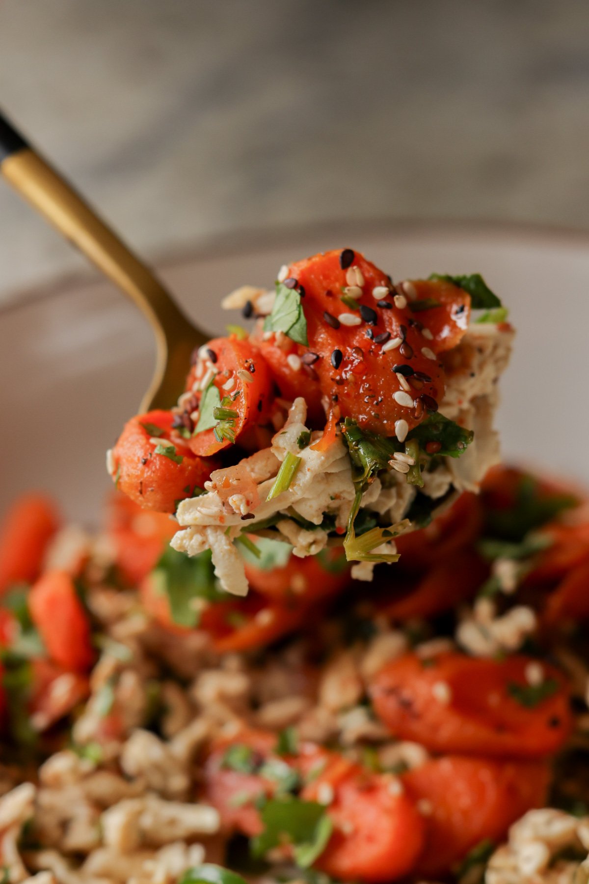 spooning a bite of shredded tofu topped with roasted carrots