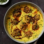 pan of kadhi pakora next to a bowl of cilantro