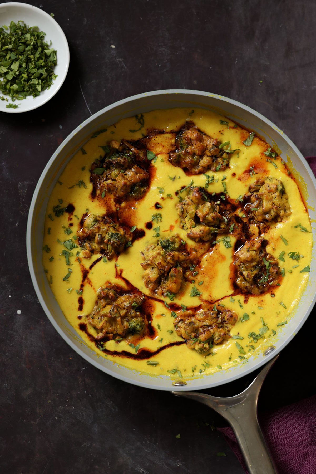 pan of kadhi pakora next to a bowl of cilantro