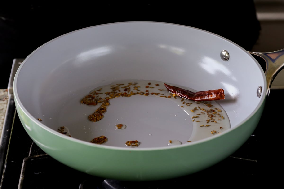 adding a red chili to the pan of roasted spices
