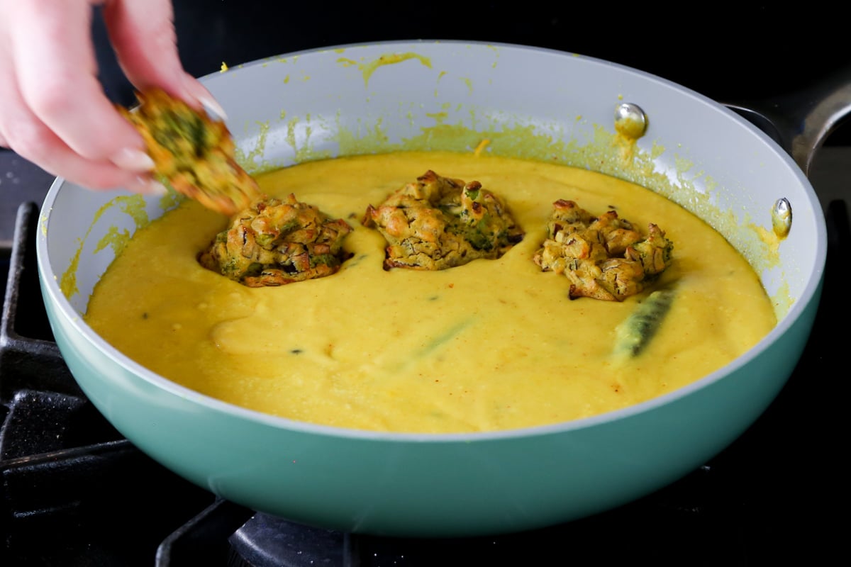 adding pakora to the pan of curry sauce